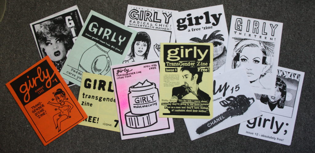 A montage of 11 copies of Simon Murphy/Mona Compleine's Girly trans zine from the 1990s, folded A4, bold graphics, some hand-coloured, some on coloured paper