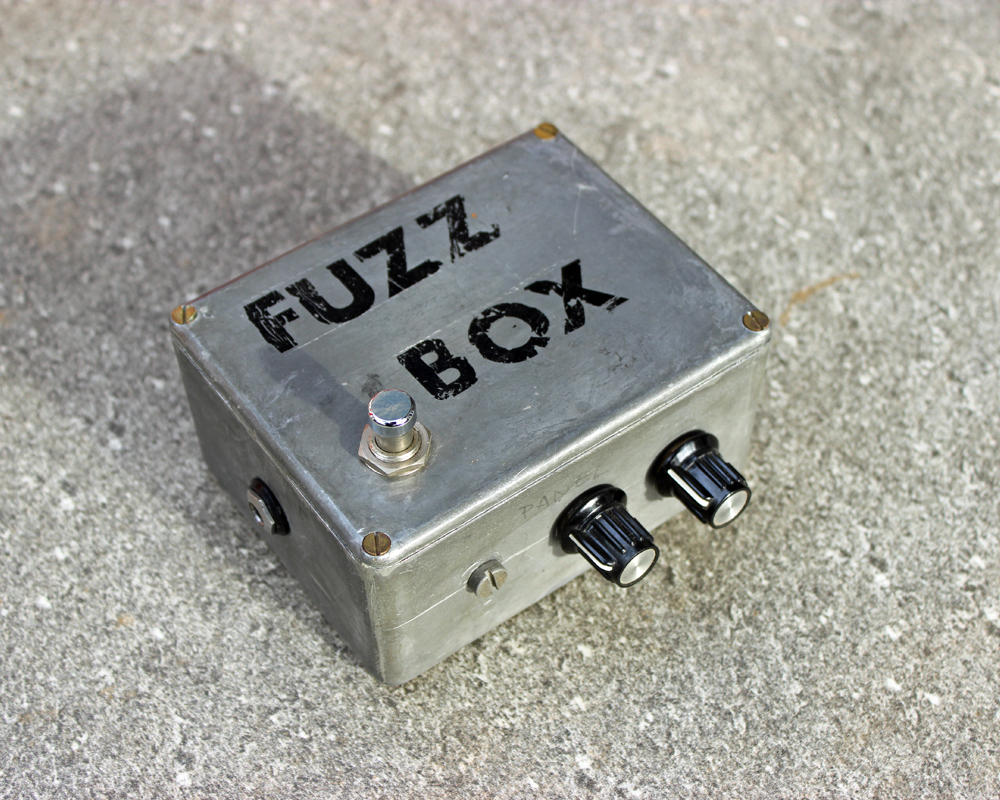 Vintage metal electronic project box with black FUZZ BOX lettering on top, knobs and a switch, looks rough and home made