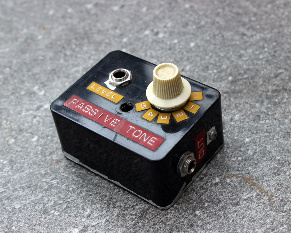 A hand made electronic tone control: small black metal box, a knob, an input and red and yellow dymo labelling