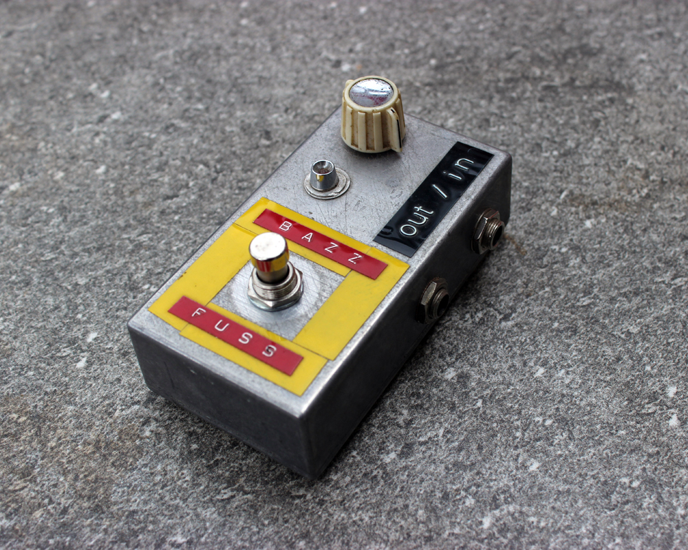 A hand made electronic fuzz pedal: small and neat metal enclosure, a knob, a light, a switch, yellow tape and dymo labels