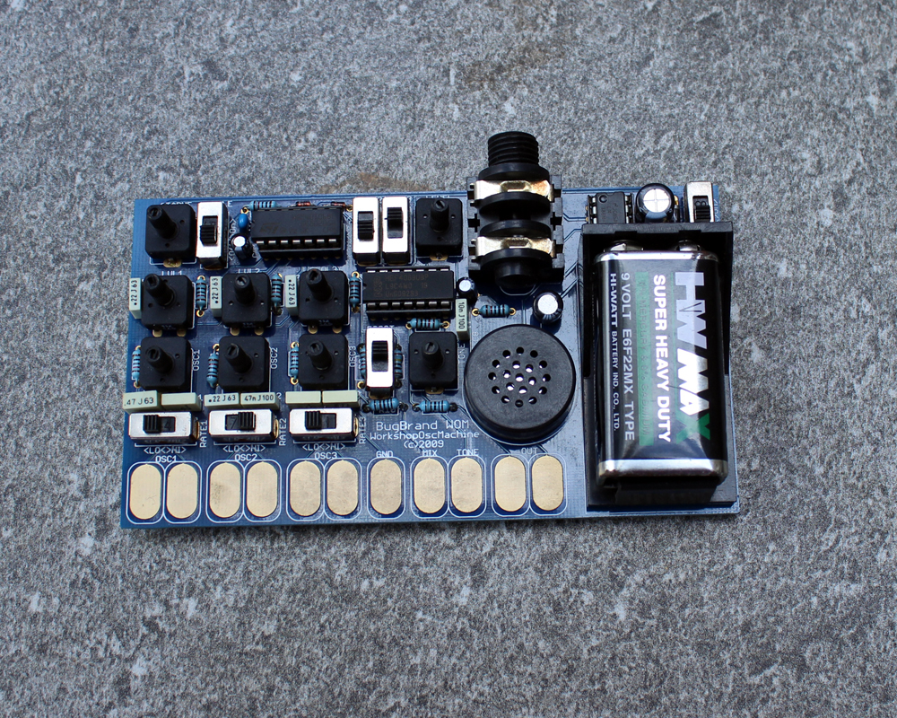 A hand made electronic musical device: a big battery, circuitboard and components and finger pads at the bottom