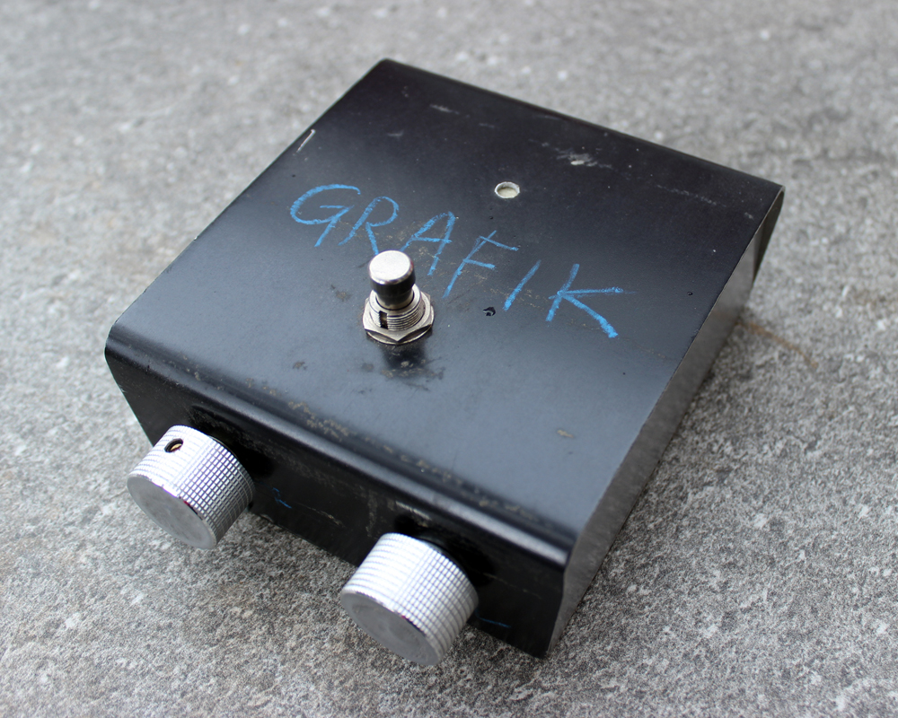 A hand made electronic pedal: extremely basic design, black metal with a switch on top, two knobs on the front, the word Grafik written roughly on top