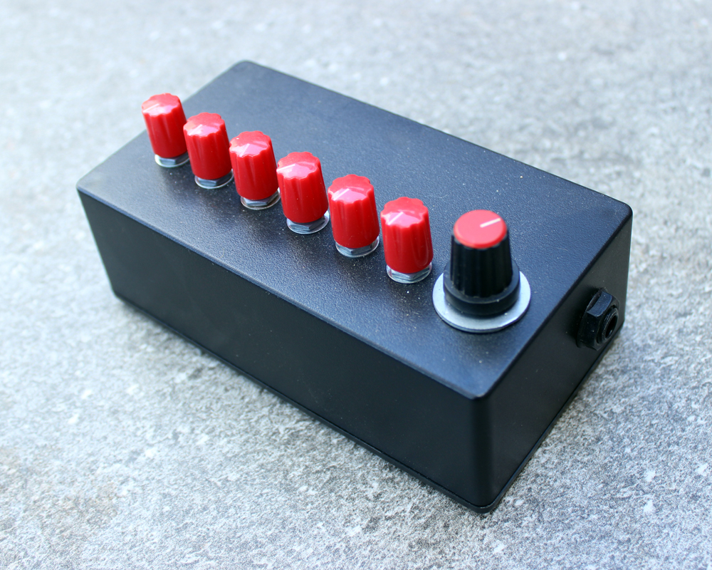 A hand made electronic effects box: black enclosure, six red knobs and a big red and black knob at the end. Looks like something Kraftwerk would use.