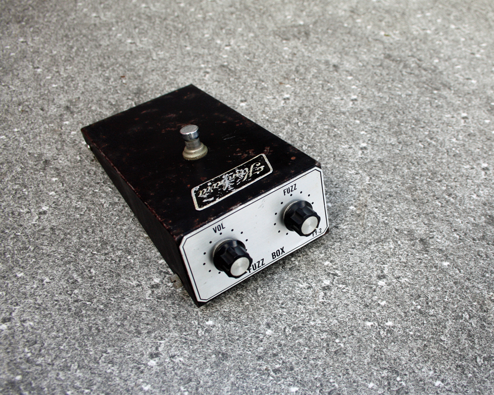 Vintage guitar fuzz pedal, metal, wedge-shaped with steel faceplate reading FUZZ BOX, two knobs on the front and a switch on top