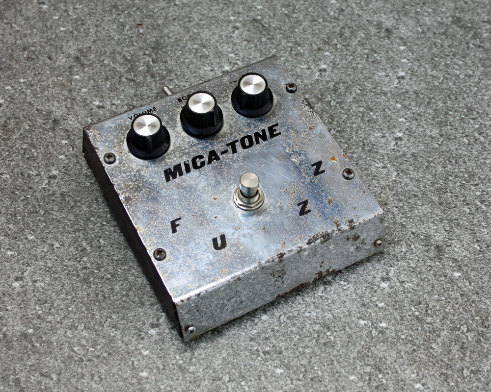 Vintage guitar fuzz pedal, metal, chrome finish, wedge-shaped, three knobs, foot switch on top and screen-printed brand name