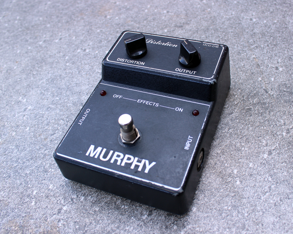 A hand made distortion pedal in black metal with white text, knobs and a switch