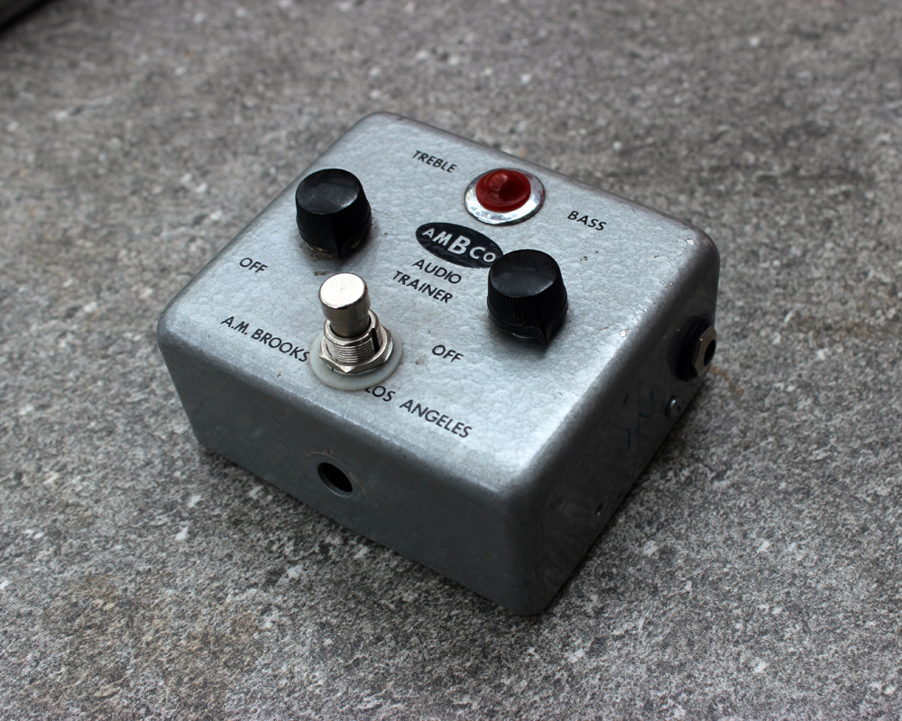 A hand-made fuzz pedal in a vintage metal enclosure with printed graphics, two knobs, a light and a switch, the word Ambco is printed in the middle