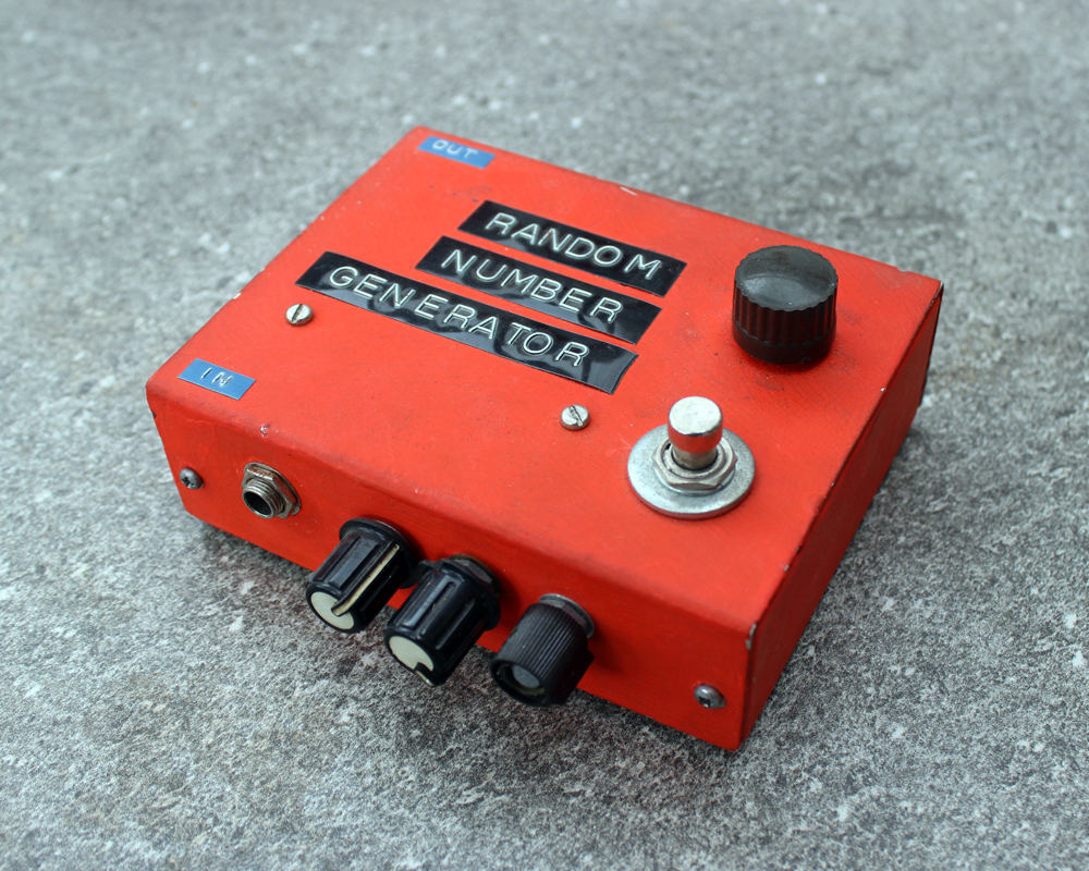 A hand made electronic pedal: red painted metal enclosure, black dymo tape labels, black plastic knobs