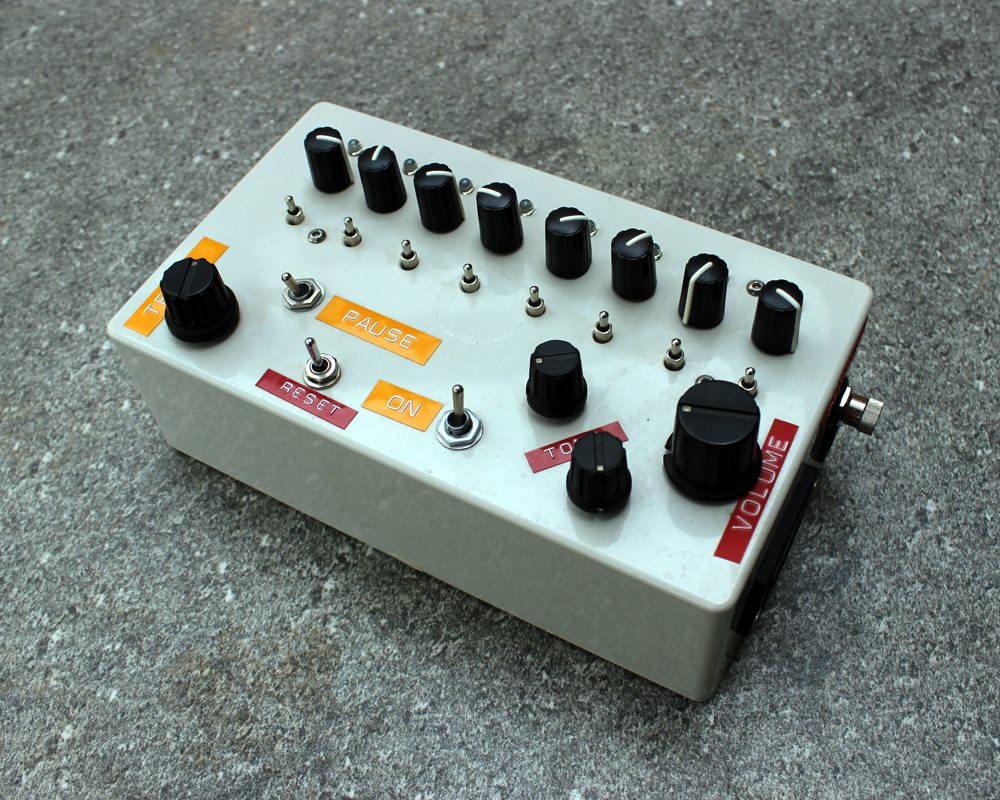 A hand made electronic sequencer, grey plastic enclosure, many knobs and switches, colourful dymo tape labels