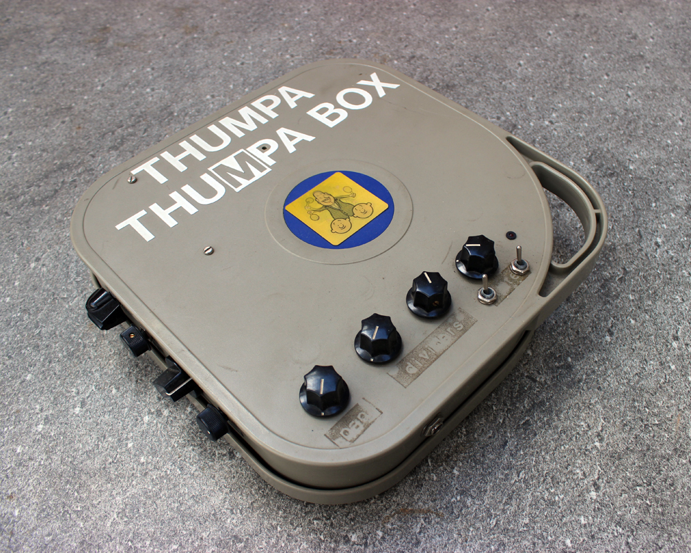 A hand made electronic pedal: plastic film box, knobs, lettering, lenticular of a bald man gleefully thumping two other bald men