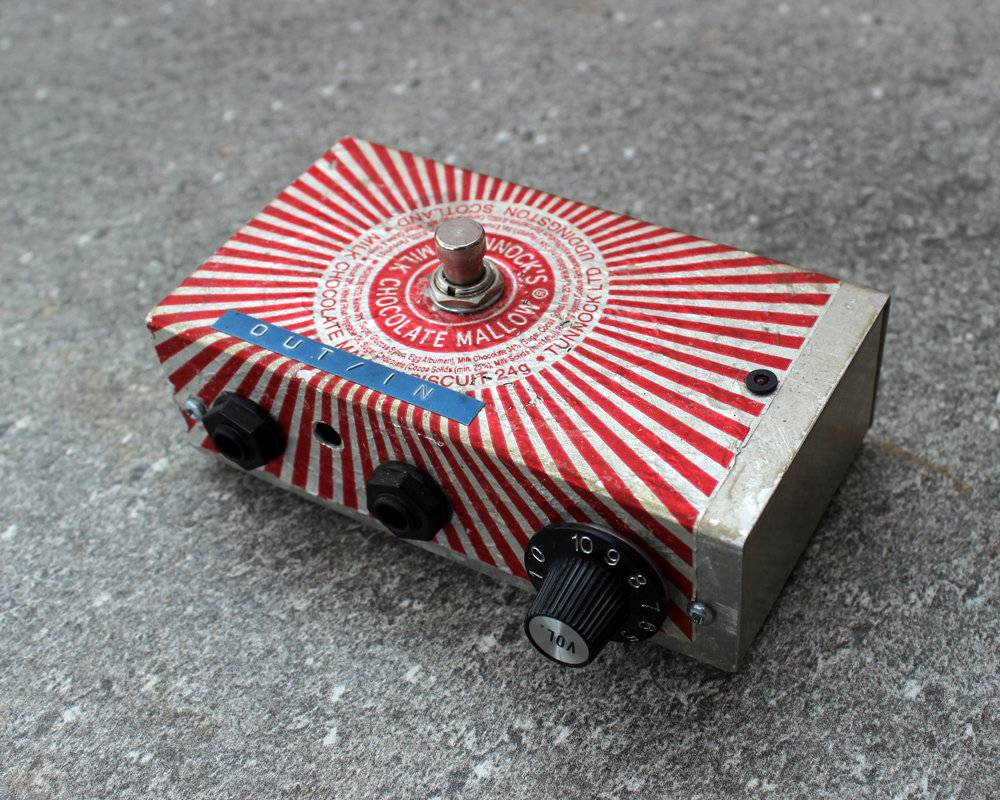 A hand made electronic pedal: metal, covered in a Tunnocks Tea Cake wrapper, dymo tape, knobs