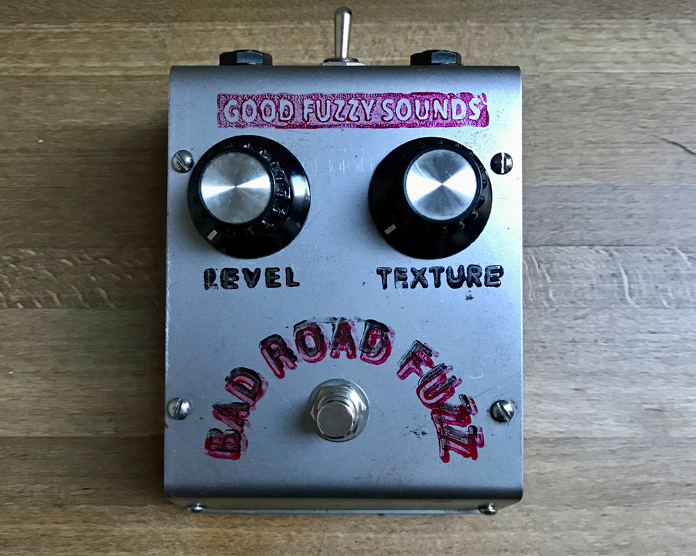 Good Fuzzy Sounds Bad Road fuzz pedal prototype, a metal box with hand-stamped graphics, knobs, switches, screw-heads, it looks like a cross face